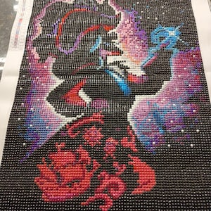 May include: Diamond painting art in progress, featuring a colorful design of a figure against a black background. The artwork uses small, sparkling gems in shades of red, pink, purple, and blue. The canvas measures 30 x 40 cm.