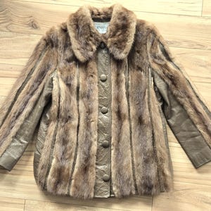 May include: A vintage brown fur jacket with a leather-like material on the sleeves and front panels. The jacket has a button-up closure and a fur collar. The fur is a mix of light and dark brown tones.
