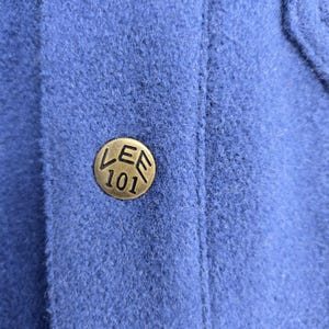 May include: Close-up of a blue fabric with a brass-colored button. The button is round with the text "LEE 101" embossed on it. The fabric has a textured appearance.