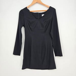 May include: A black long-sleeve dress featuring a scalloped neckline and a fitted bodice. The garment has a straight skirt silhouette and a vertical zipper closure at the center back, displayed on a wooden hanger against a plain white background.