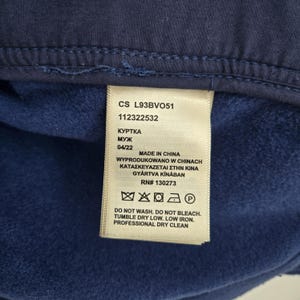 May include: A dark blue garment interior featuring a cream-colored care label with the text CS L93BVO51, 112322532, MADE IN CHINA, RN# 130273, and care instructions including DO NOT WASH, DO NOT BLEACH, TUMBLE DRY LOW, LOW IRON, PROFESSIONAL DRY CLEAN.