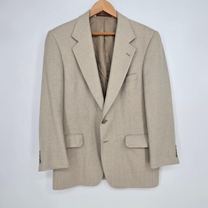 May include: A beige blazer with a textured weave, featuring a single-button front closure, notched lapels, two flap pockets at the waist, one chest pocket, and three buttons on each sleeve cuff, all lined with a smooth brown interior fabric.