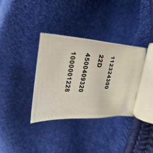 May include: A white tag with black text against a blue fabric background. The tag displays the numbers 1000001228, 4500409320, 22D, and 112324300. The fabric is a solid, deep blue color.