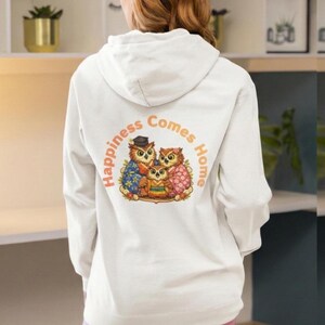 以下が含まれることがあります： 背中に3羽のフクロウが描かれたカラフルなグラフィックが特徴の白いパーカー。 フクロウは様々な衣装を着ており、「Happiness Comes Home」の文字が円形にプリントされています。 パーカーにはドローストリングフードが付いています。