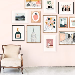 May include: A pink wall gallery with framed artwork, including a champagne bottle, a strawberry, a cityscape, a hot air balloon, and a woman riding a horse. The gallery is decorated with a vintage armchair.