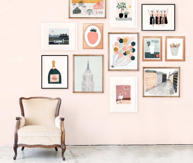 May include: A pink wall gallery with framed artwork, including a champagne bottle, a strawberry, a cityscape, a hot air balloon, and a woman riding a horse. The gallery is decorated with a vintage armchair.