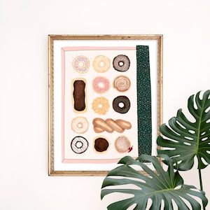 May include: A framed print of a colorful illustration of various donuts and pastries. The print is on a pink background with a green and gold stripe on the right side. The print is framed in gold.
