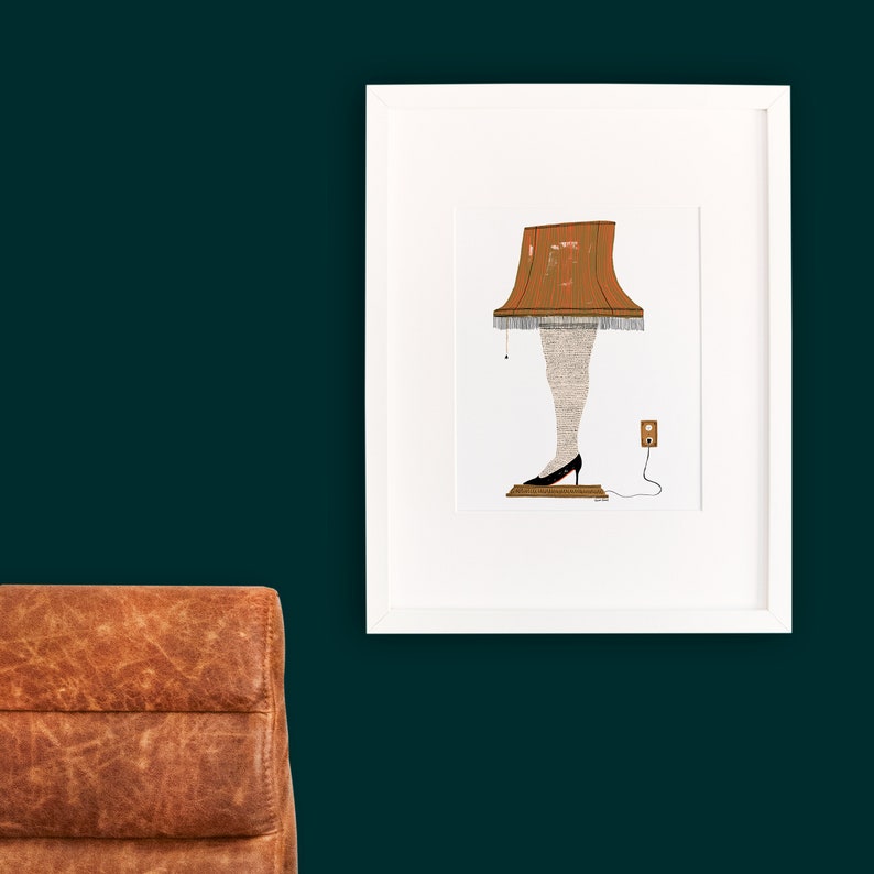 May include: A white framed print of a lampshade with legs wearing a black shoe. The lampshade is brown with a white trim and is plugged into an outlet. The print is on a dark green wall.