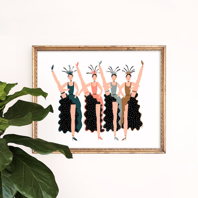May include: Five women in black, green, and blue dresses with feathered headbands are kicking their legs up in the air. They are all smiling and looking at the viewer. The background is white.