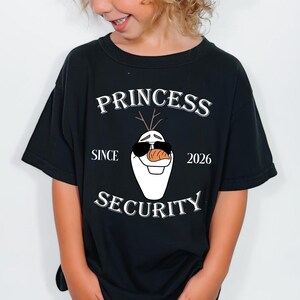 以下が含まれることがあります： 「PRINCESS SECURITY SINCE 2026」の文字とサングラスをかけたオラフのグラフィックがプリントされた黒いTシャツ。子供はまた、グレーのメッシュバックとタンのつばが付いたトラッカーハットをかぶっています。