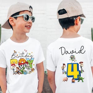 Pode incluir: Camiseta branca com um gr&aacute;fico colorido "Birthday BOY" com personagens de desenhos animados. A parte de tr&aacute;s da camisa tem o nome "David" e o n&uacute;mero "4" com mais personagens de desenhos animados. A camisa &eacute; usada por uma crian&ccedil;a.