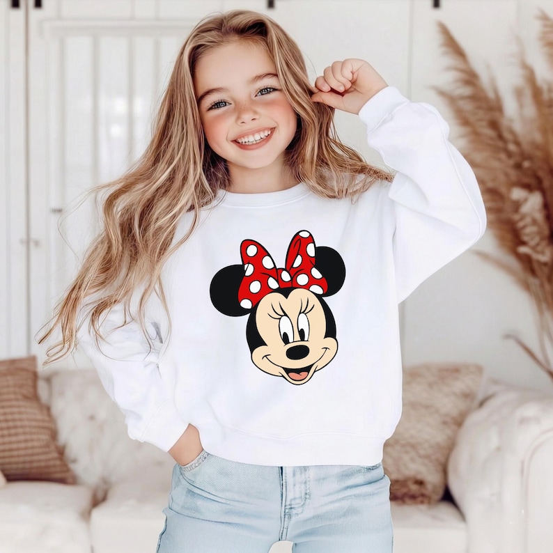 May include: White sweatshirt with a Minnie Mouse design. The graphic shows Minnie's face, a red bow with white spots, and black ears. The sweatshirt is a long-sleeved, casual top.