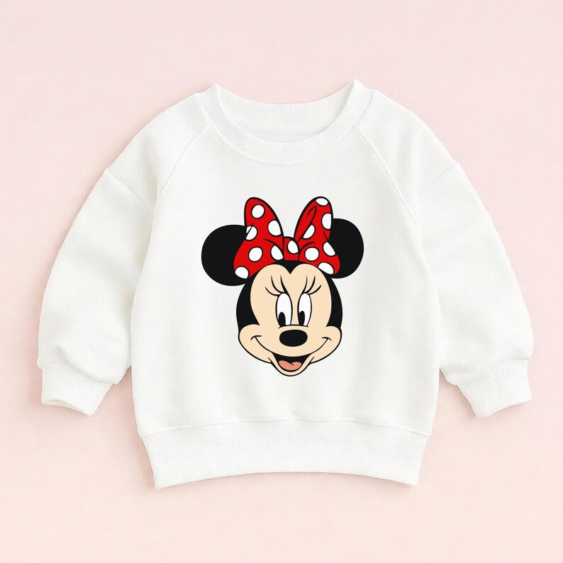 May include: White sweatshirt with a Minnie Mouse graphic. The graphic depicts Minnie's face, a red bow with white polka dots. The sweatshirt has long sleeves and a crew neck.