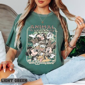 May include: Light green t-shirt with a graphic of Disney characters, including Mickey and Minnie Mouse, Donald and Daisy Duck, and Goofy. The design includes the text "Animal Kingdom" and "Walt Disney World".