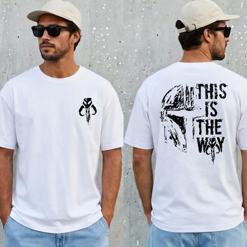 May include: A white short-sleeved t-shirt featuring a small black graphic of a helmet on the left chest. The back of the shirt displays a large black graphic of a helmet with the text "THIS IS THE WAY" in a distressed, bold font.