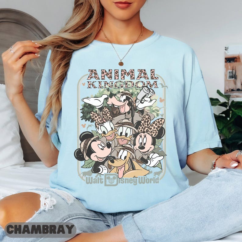 May include: Pale blue t-shirt with a graphic of Disney characters, including Mickey and Minnie Mouse, Donald Duck, and Goofy. The shirt has the text "ANIMAL KINGDOM" and "Walt Disney World". The shirt is made of a soft material.