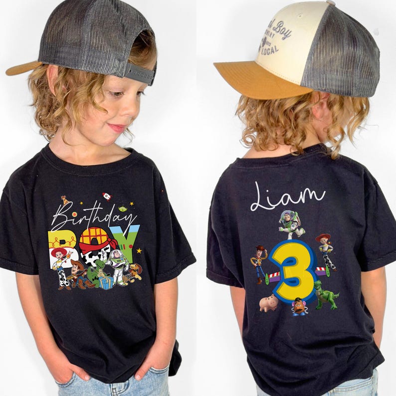 Pode incluir: Camiseta preta com um gr&aacute;fico colorido "Birthday Boy" com personagens de Toy Story. A parte de tr&aacute;s da camisa tem o nome "Liam" e o n&uacute;mero "3" com mais personagens de Toy Story. A crian&ccedil;a est&aacute; usando um bon&eacute; de caminhoneiro.