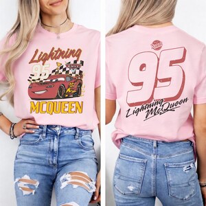 Puede incluir: Camiseta rosa claro con dise&ntilde;o de Rayo McQueen de la pel&iacute;cula Cars. La parte delantera muestra a Rayo McQueen, el n&uacute;mero 95 y texto. La parte trasera tiene el n&uacute;mero 95 y la frase "Lightning McQueen".