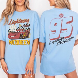 Puede incluir: Camiseta azul claro con un dise&ntilde;o de Rayo McQueen de la pel&iacute;cula Cars. La parte delantera muestra el coche con el texto "Lightning 95 McQueen". La parte trasera tiene un gran "95" y el texto "Lightning McQueen".