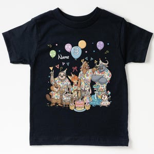 K&ouml;nnte beinhalten: Marineblaues Kinder-T-Shirt mit einer bunten Geburtstagsparty-Szene. Die Illustration zeigt Zeichentricktiere, Luftballons und Konfetti. Die Zahl "3" und das Wort "Name" sind ebenfalls zu sehen.