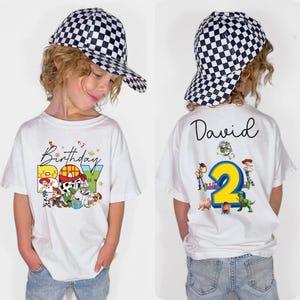 Pode incluir: Uma camiseta branca com a frase "Birthday Boy" e personagens de desenhos animados. A parte de tr&aacute;s da camiseta tem o nome "David" e o n&uacute;mero "2" com mais personagens de desenhos animados. A crian&ccedil;a est&aacute; usando um bon&eacute; de beisebol xadrez preto e branco.