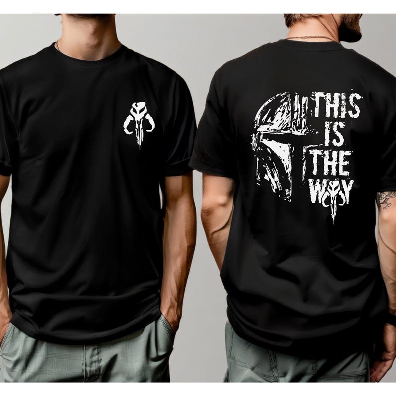 May include: A black short-sleeved t-shirt featuring a white graphic of a helmet symbol on the front left chest. The back displays a large white distressed graphic of a helmet and the text THIS IS THE WAY with a small symbol below the text.