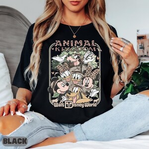 May include: Black t-shirt with a graphic of Disney characters, including Mickey Mouse, Minnie Mouse, Donald Duck, Daisy Duck, Goofy, and Pluto. The design includes the text "ANIMAL KINGDOM" and "Walt Disney World" in a decorative frame.