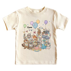 K&ouml;nnte beinhalten: Cremefarbenes Kinder-T-Shirt mit einer farbenfrohen Geburtstagsparty-Szene mit Zeichentricktieren. Das Design umfasst Luftballons, eine Torte und die Zahl "3". Das Wort "Name" ist ebenfalls sichtbar. Ein lustiges und festliches Design.