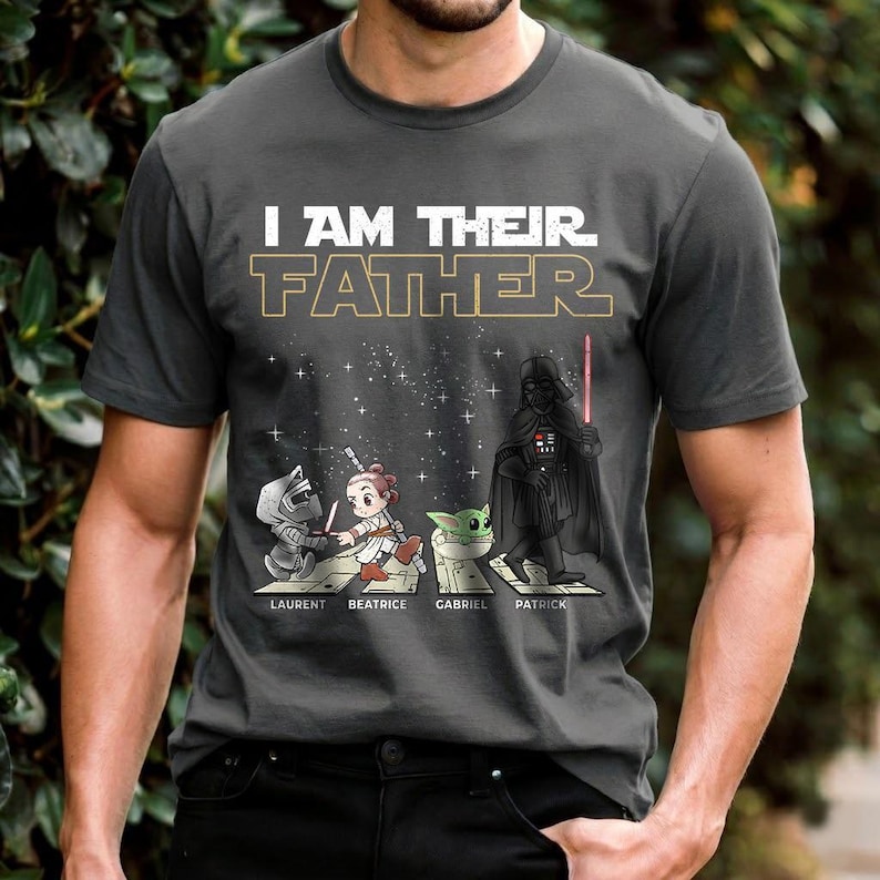 May include: Dark gray t-shirt with the text "I AM THEIR FATHER" in white and gold. The shirt features cartoon illustrations of characters, including Darth Vader, with the names Laurent, Beatrice, Gabriel, and Patrick below.