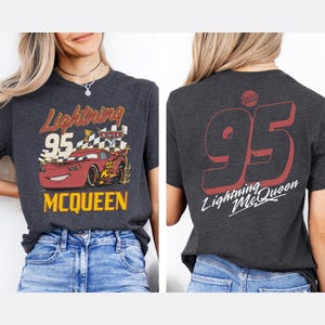 Puede incluir: Camiseta gris oscuro con Lightning McQueen de la pel&iacute;cula Cars. El gr&aacute;fico frontal muestra a McQueen con el n&uacute;mero 95, el texto "Lightning" y "McQueen". La parte posterior de la camiseta muestra un gran "95" rojo y "Lightning McQueen" en blanco.