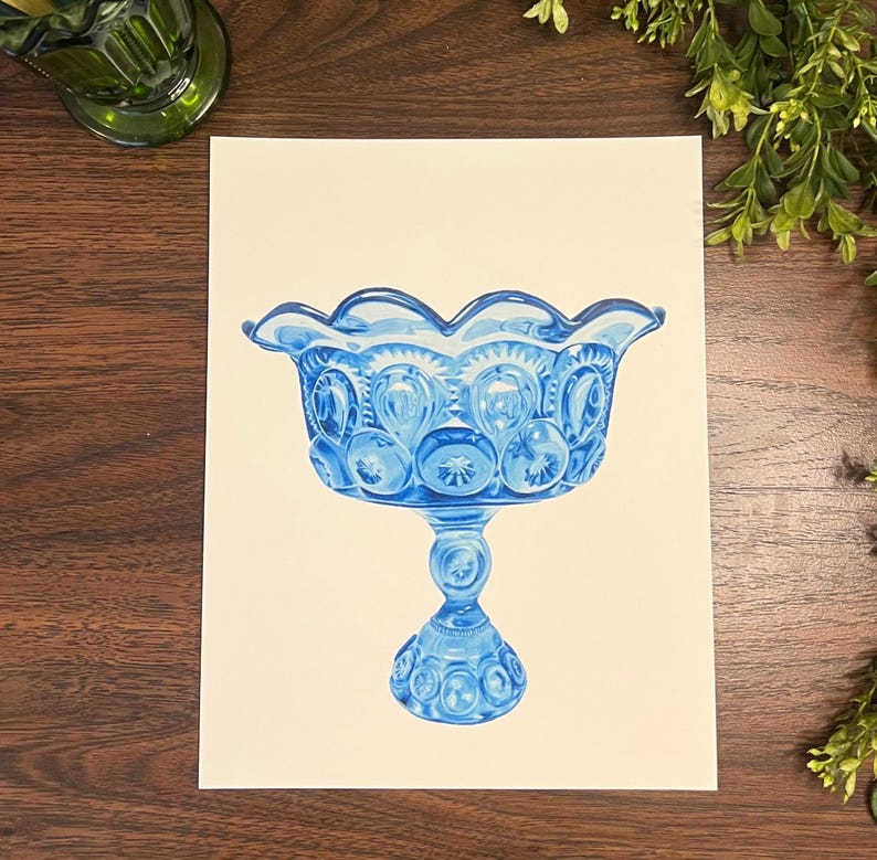K&ouml;nnte beinhalten: Eine blaue Glas-Fu&szlig;schale mit gewelltem Rand. Die Schale hat ein Stern- und Mondmuster und steht auf einem detaillierten Sockel. Die Schale ist ein dekoratives St&uuml;ck, wahrscheinlich zum Servieren oder Ausstellen.