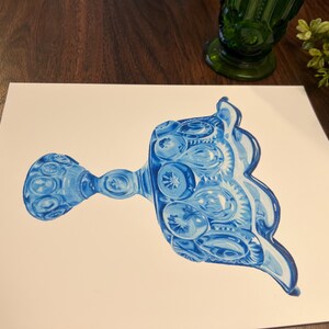K&ouml;nnte beinhalten: Ein Aquarellgem&auml;lde eines blauen Glas-Serviertellers mit detailliertem Muster. Der Teller befindet sich auf einer wei&szlig;en Oberfl&auml;che, mit einer gr&uuml;nen Glasvase und Gr&uuml;nzeug im Hintergrund. Der Teller hat einen Griff und einen dekorativen Rand.