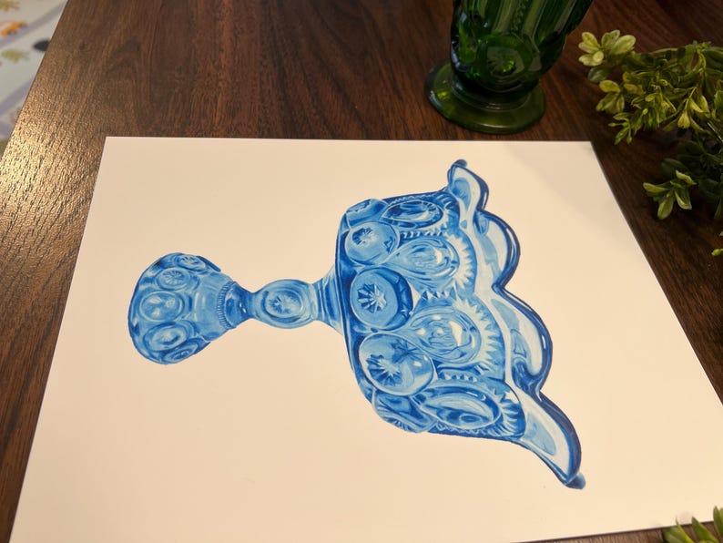 K&ouml;nnte beinhalten: Ein Aquarellgem&auml;lde eines blauen Glas-Serviertellers mit detailliertem Muster. Der Teller befindet sich auf einer wei&szlig;en Oberfl&auml;che, mit einer gr&uuml;nen Glasvase und Gr&uuml;nzeug im Hintergrund. Der Teller hat einen Griff und einen dekorativen Rand.