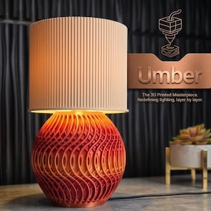May include: A 3D-printed table lamp with a beige, vertically-lined lampshade and a red and orange patterned base. The lamp is labelled "Umber" and the text reads "The 3D Printed Masterpiece. Redefining lighting, layer by layer."