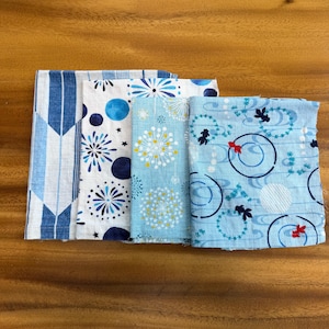 Puede incluir: Cuatro muestras de tela rectangulares dispuestas una al lado de la otra. La primera presenta flechas azules y blancas. La segunda tiene círculos y estallidos azules. La tercera es azul claro con motivos florales amarillos y blancos. La cuarta muestra peces dorados.