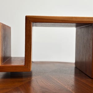 Puede incluir: Una estanter&iacute;a de madera con un dise&ntilde;o abierto &uacute;nico. La estanter&iacute;a est&aacute; construida con madera de tonos c&aacute;lidos, con un marco rectangular y un soporte vertical. El dise&ntilde;o es moderno y minimalista, adecuado para exhibir libros o decoraci&oacute;n.