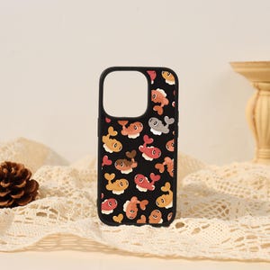 May include: A black smartphone case featuring a repeating pattern of small, stylized fish in shades of orange, red, brown, and gray. Each fish is depicted with a rounded body and a white base, creating a consistent graphic design across the surface.