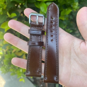 May include: A pair of brown leather watch straps with silver-colored buckles. The straps are a rich, dark brown color with visible stitching along the edges. The watch straps are new and unworn.