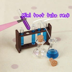 May include: A miniature laboratory set with a brown wooden test tube rack, glass test tubes filled with blue liquid, and a flask with a cork. The text "Mini test tube rack" is visible.