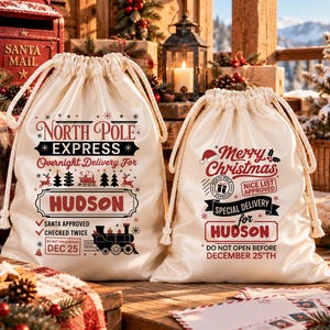 May include: Two cream-colored drawstring canvas bags with festive holiday graphics. The left bag features North Pole Express text, a train, and the name Hudson. The right bag displays Merry Christmas, Nice List Approved, and Hudson.