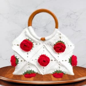 Peut inclure: Sac à main en crochet blanc orné d'appliqués de roses rouges et d'une anse en bois. Le sac présente un motif géométrique et est orné de plusieurs roses rouges vives, ajoutant une touche florale. L'anse est en bois naturel.