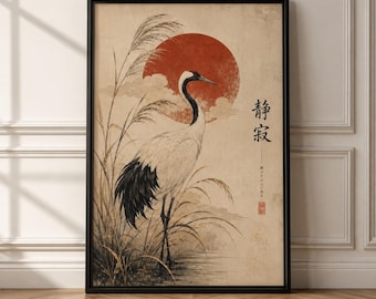 以下が含まれることがあります： 高い草の中に立つ白と黒の鶴を描いた額入りアートプリント。ベージュの質感のある背景に、大きな赤い太陽が描かれています。作品には黒い日本語の書道文字と小さな赤い印章が含まれています。