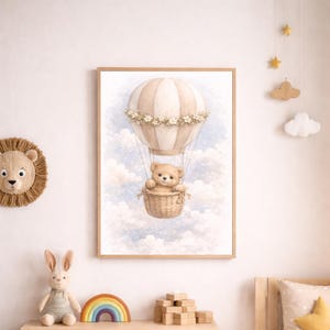 May include: A framed wall art print featuring a light brown teddy bear sitting in a woven basket attached to a beige hot air balloon decorated with small white flowers, all floating against a soft, pale blue sky filled with fluffy white clouds.