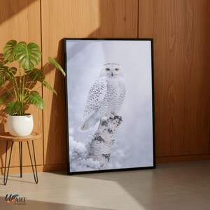May include: A framed print of a snowy owl perched on a snow-covered tree trunk. The owl has white feathers with black spots and yellow eyes. The background is a snowy landscape. The frame is black.