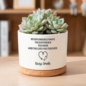 May include: A white ceramic planter with a bamboo saucer containing a green succulent. The planter features black text reading "NEVER UNDERESTIMATE THE DIFFERENCE YOU MADE AND THE LIVES YOU TOUCHED," a heart-shaped stethoscope icon, and "Nurse Smith."