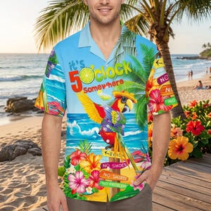 May include: A short-sleeved, button-down shirt with a tropical beach scene. The shirt features a parrot wearing a hat, palm trees, flowers, and the text "It's 5 O'Clock Somewhere." The shirt has a light blue background.