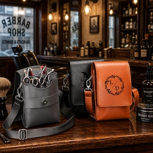 May include: Three rectangular barber tool holsters with adjustable straps, one gray and two brown, featuring a flap closure with a snap button. The front of the brown holster displays a circular wreath design with the letters L and D in the center.