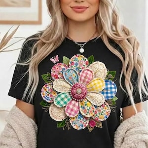 May include: Black t-shirt featuring a large, colorful flower design. The flower is composed of various patterned fabric circles, including floral, gingham, and solid colors. A small butterfly is visible near the flower.