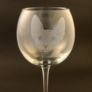 May include: A clear glass wine glass with an etched image of a hairless cat on the front.