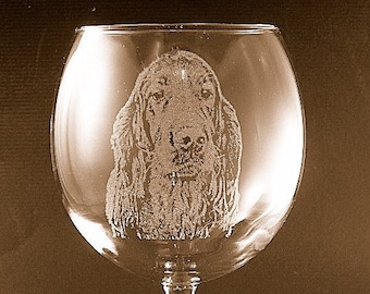 May include: A clear glass wine glass with a round bowl and a long stem. The glass has an etched image of a brown and black dog's head.